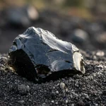 Lesklý černý přírodní obsidián s ostrými odrazivými hranami na sopečné půdě